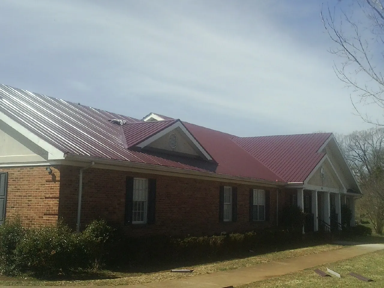 Red metal roof with gabled entries on a long brick building, from a Hail Damage Roof Repair job in Tempe